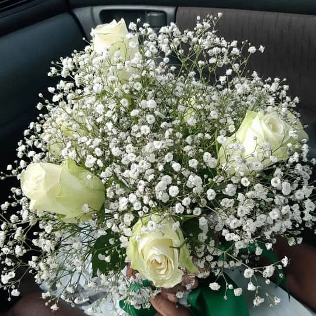 A bridal bouquet of white roses and baby's breath, tied with green ribbon